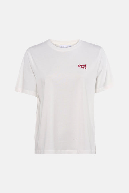 T-shirt blanc à manches courtes de VILA®, avec petit imprimé texte rouge, porté avec un jean ample et des escarpins noirs.