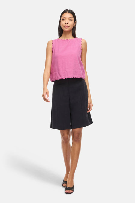 Roze mouwloze blouse van VILA® met geschulpte randen, gedragen met zwarte shorts en zwarte open schoenen.