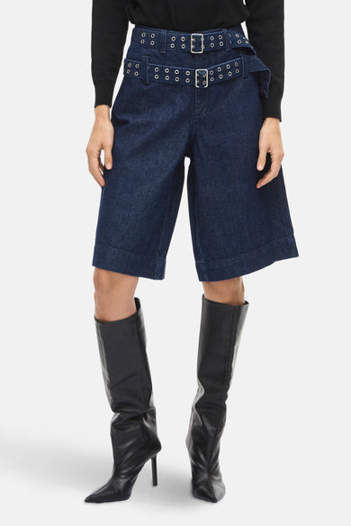 Short de denim bleu marine de VILA®, avec une ceinture double et porté avec des bottes noires et un gilet.