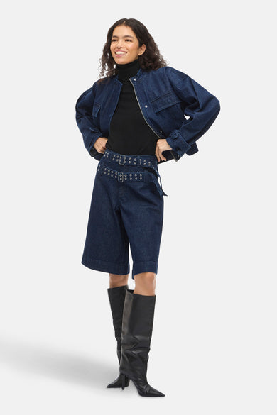 Donkerblauwe denim short van VILA®, met dubbele riem en gedragen met zwarte laarzen en coltrui.
