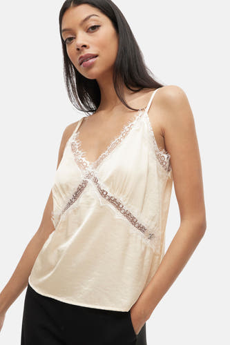 Ecru mouwloze blouse van VILA, met kanten details langs de halslijn en zijkanten, gecombineerd met een zwarte broek.