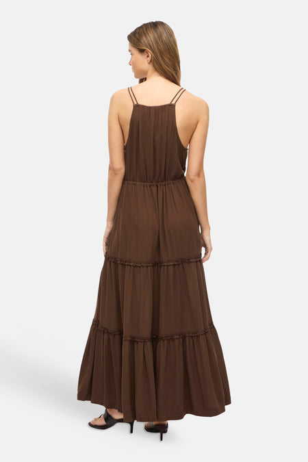 Robe marron sans manches de VILA® avec fines bretelles, taille élastique et jupe à volants, portée avec des sandales foncées, dos.