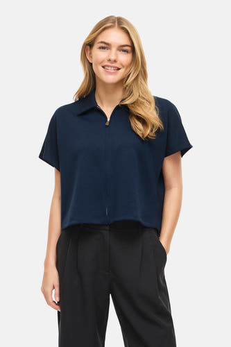 Blauwe sweater van VILA®, met korte mouwen en een ritssluiting aan de voorkant, gecombineerd met een zwarte pantalon.
