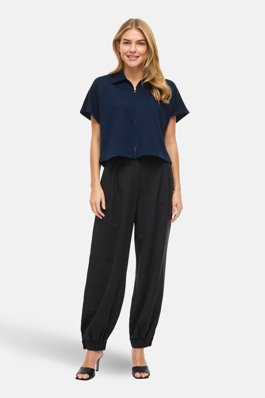Blauwe sweater van VILA®, met korte mouwen en een ritssluiting, gecombineerd met een zwarte pantalon en hakken.