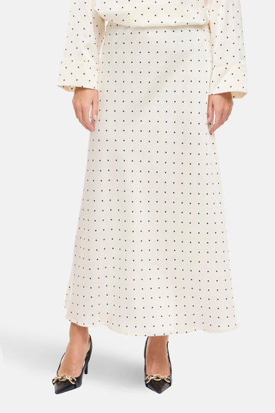 Lange ecru rok van VILA®, met zwarte stippen en zwarte pumps met gouden details.
