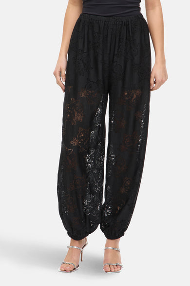 Pantalon noir de VILA®, avec un motif floral et une ceinture élastique, porté avec des baskets argentées.