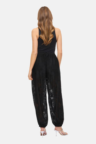Pantalon noir de VILA® avec ce taille élastique et une bordure à fleurs, porté avec un haut noir et des talons argentés.