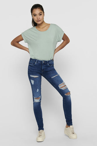 Vrouw met groene top en gescheurde jeans, staand.
