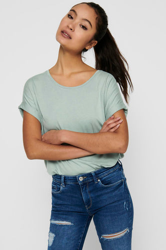 Femme avec les bras croisés dans un t-shirt vert et des pantalons de travail bleus.