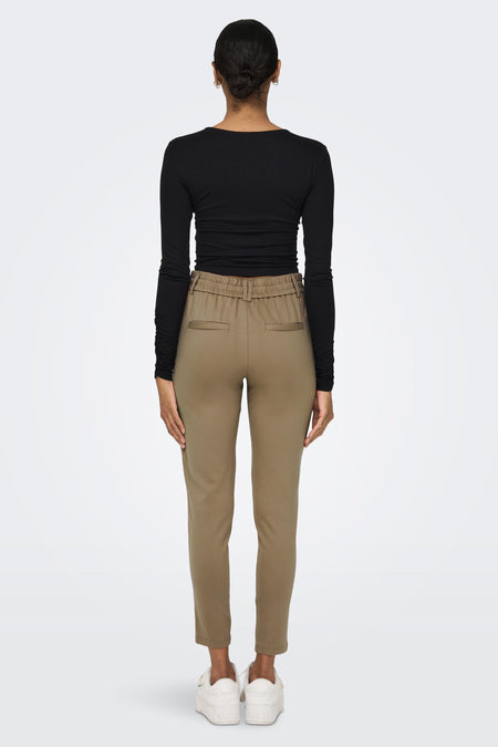 Bruine chino broek van ONLY® met elastische taille, achterzakken en slim fit, getoond van achteren op model in zwarte top en witte sneakers