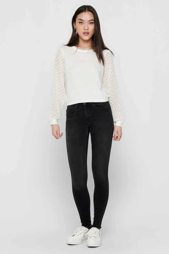 Zwarte skinny jeans van ONLY, gecombineerd met een witte blouse met structuurdetails en witte schoenen.
