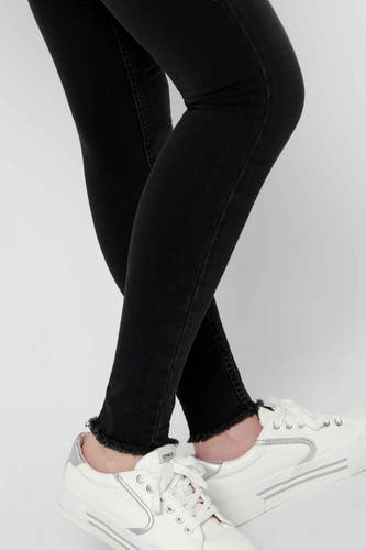 Zwarte skinny jeans van ONLY, met gerafelde zoom en gecombineerd met witte sneakers.
