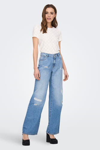 Wit T-shirt van JDY, met korte mouwen en een patroon van kleine gaatjes, gecombineerd met wijde, gescheurde jeans en zwarte plateauzolen.
