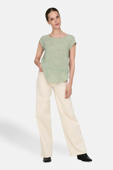 Groene blouse met korte mouwen van ONLY, met een wit bladmotief, gedragen met een crèmekleurige pantalon en zwarte schoenen.
