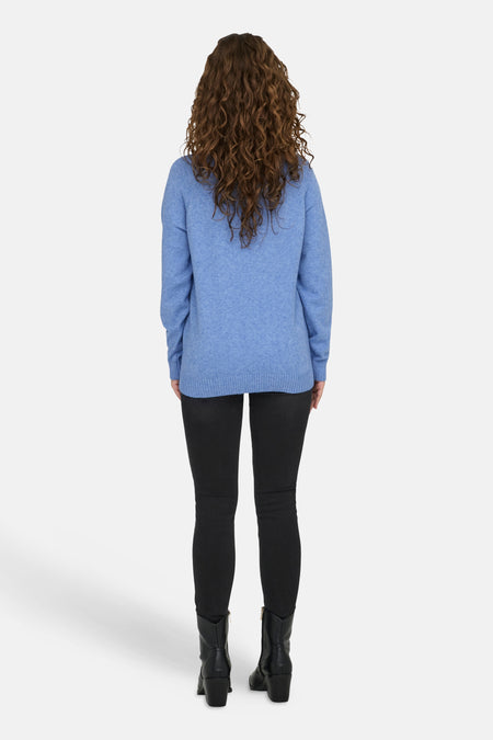 Blauwe trui met ronde hals van ONLY, gezien van achteren, met krullend haar, zwarte broek en laarzen.
