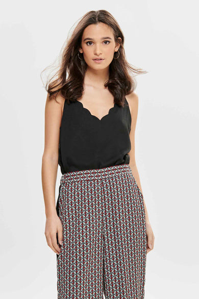Blouse sans manches noire d'ONLY, avec une ligne de col sculptée, portée avec un pantalon à motif géométrique.