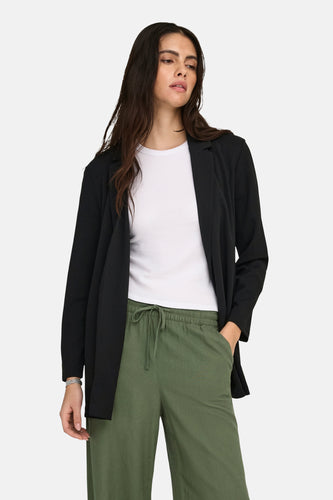 Femme en blazer noir, chemise blanche et pantalon vert.