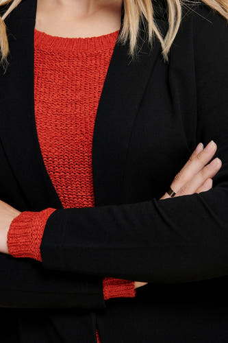 Zwarte blazer van JDY, met gekruiste armen en een oranje gebreide trui eronder.
