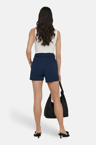 Blauwe short van JDY, met elastische tailleband en achterzak, gedragen met een wit topje en zwarte hakken.

