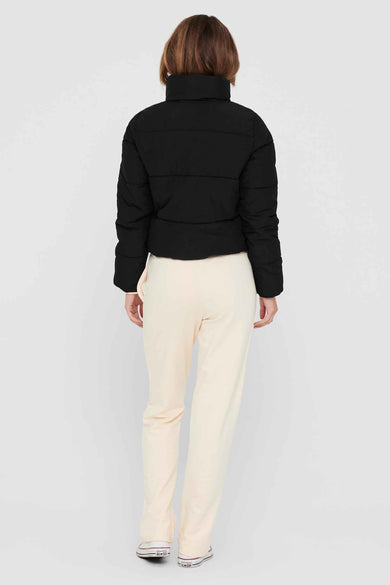 Zwarte korte jas van ONLY, met hoge kraag en gedragen met crèmekleurige broek en witte sneakers.
