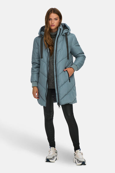 Blauwe lange jas van JDY, met diagonale stiksels en een capuchon, gecombineerd met een grijze trui en zwarte legging.
