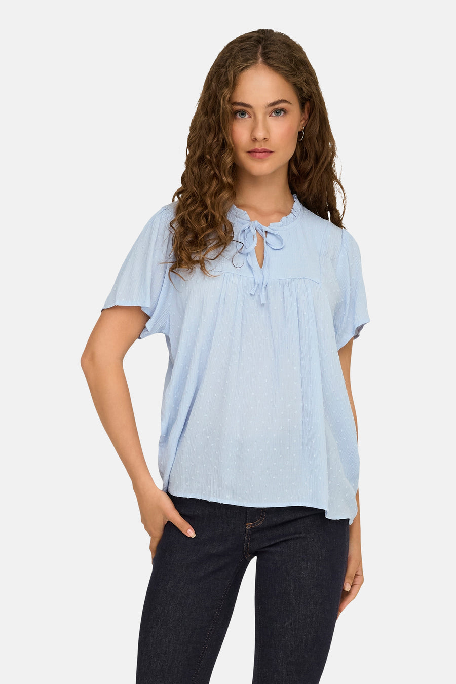 Blauwe blouse met korte mouwen van JDY, met kleine stippen, een ruchekraag en strikdetails aan de hals, gedragen met een donkere jeans.