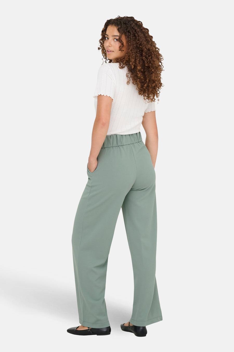 Dame draagt een wit shirt en een groene, wijde broek.