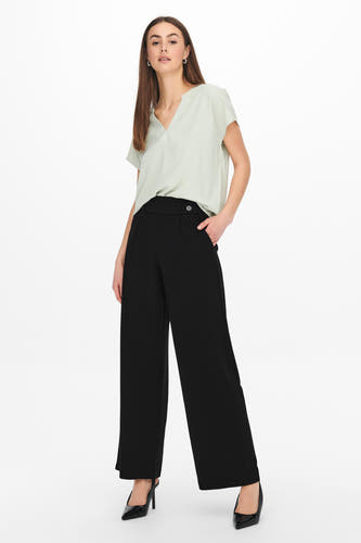 Pantalon de costume noir JDY, avec des jambes larges et un détail de nœud sur la ceinture, associé à une chemise verte claire et des baskets noires.