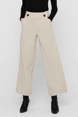 Grijze kostuumbroek van JDY, met wijde pijpen en knoopdetails in de tailleband, gecombineerd met zwarte laarsjes.
