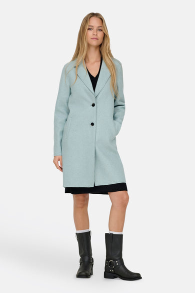 Manteau long bleu d'ONLY, avec fermeture à boutons, associé à une jupe noire et de robustes bottines noires.