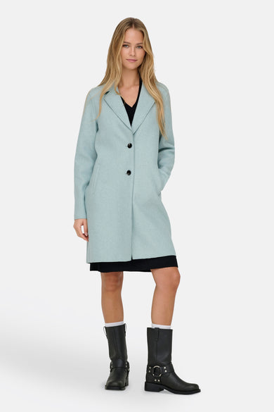 Manteau bleu d'ONLY, porté avec une jupe noire et des bottes noires robustes avec des chaussettes blanches.
