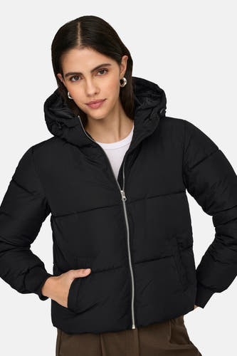 Manteau court noir de JDY, avec capuche et fermeture éclair argentée, porté sur un chemisier blanc.