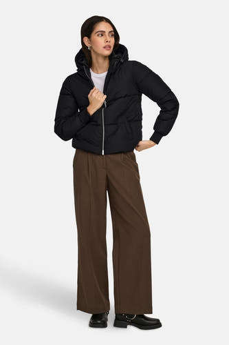 Manteau court noir de JDY, avec capuche et fermeture éclair argentée, porté avec des pantalons marron et des bottes noires.