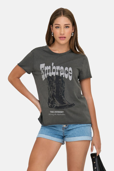 Grijs T-shirt met korte mouwen van ONLY, met print van een cowboylaars en de tekst "Embrace", gedragen met denim shorts.
