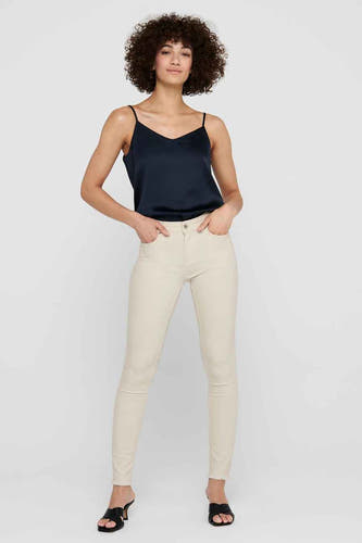 Jean skinny beige de ONLY®, porté avec un haut de soie bleu foncé et des baskets noires.