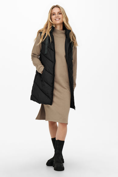 Gilet chauffant noir de JDY, porté sur une jupe beige et avec des bottes noires.