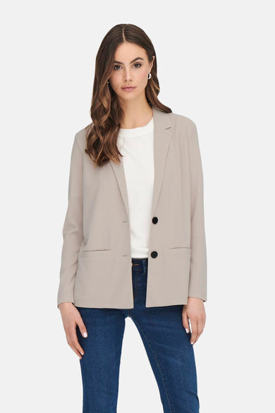 Beige blazer van JDY, met lange mouwen en zwarte knopen, gedragen over een wit T-shirt en een donkere jeans.
