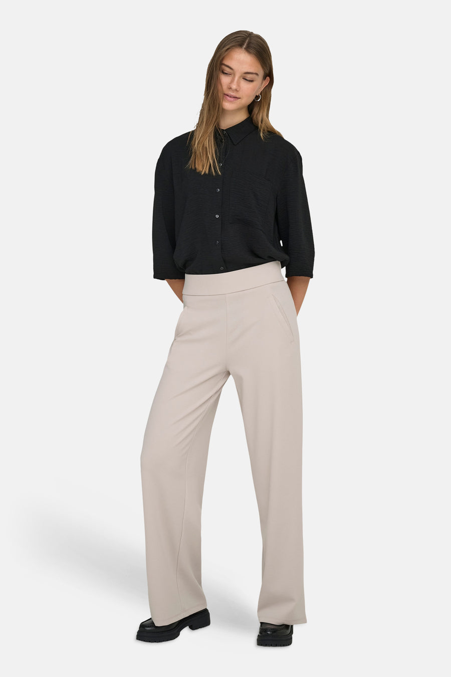 Pantalon de costume beige clair de JDY à jambes larges, porté avec un chemisier noir et des mocassins.