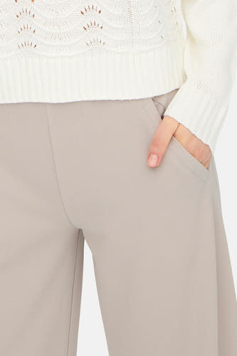 Grijze kostuumbroek van JDY, met een hand in de zak en een witte gebreide trui.
