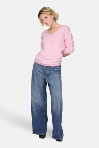 Roze V-hals trui van ONLY, gecombineerd met wijde jeans en zwarte schoenen.