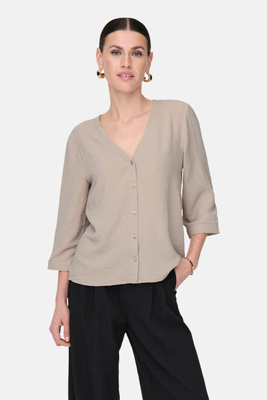 Blouse beige de JDY avec des manches trois-quarts, une fermeture à boutons et portée avec un pantalon noir large.