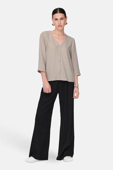 Beige blouse van JDY met driekwart mouwen, knoopsluiting en gedragen met zwarte, wijde broek.
