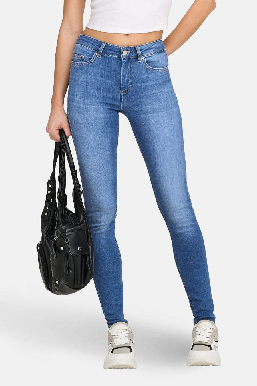 Skinny jeans van mid blue denim, van ONLY, met een zwarte tas en witte sneakers.
