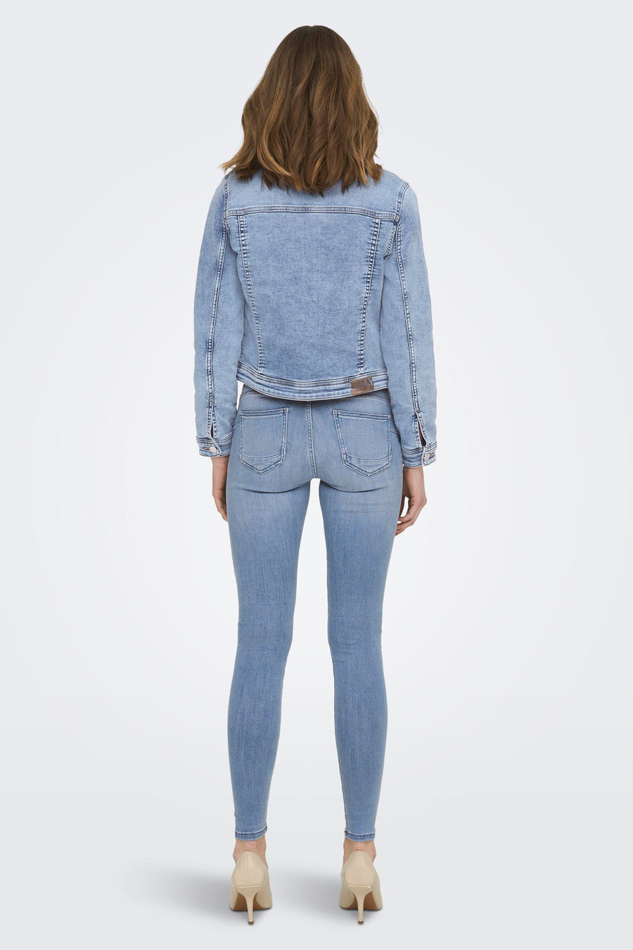 Lichtblauwe skinny jeans van ONLY, gecombineerd met een denim jack en beige pumps, gezien van achteren.
