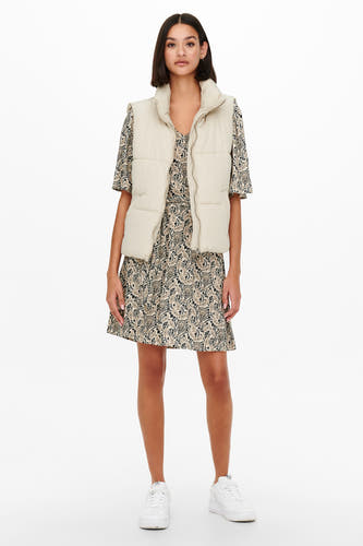 Ecru bodywarmer van JDY, gedragen over een jurk met paisleyprint en witte sneakers.