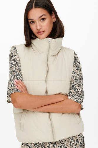 Ecru bodywarmer van JDY met een opstaande kraag en een ritssluiting, over een blouse met paisley-print.
