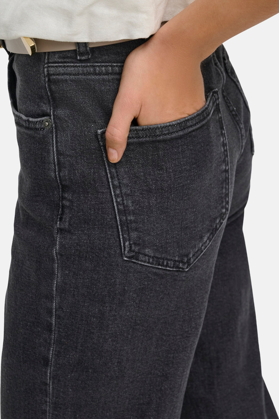 Jean large gris foncé d'ONLY, avec une main dans la poche et une ceinture blanche.