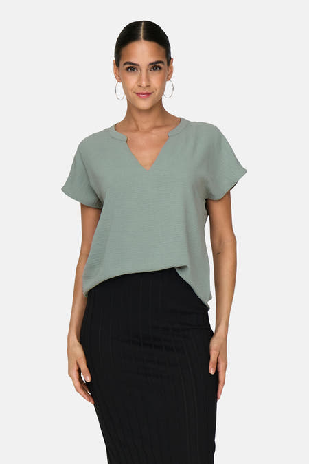 Groene blouse met korte mouwen van JDY, gedragen met een zwarte rok en zilveren oorbellen.
