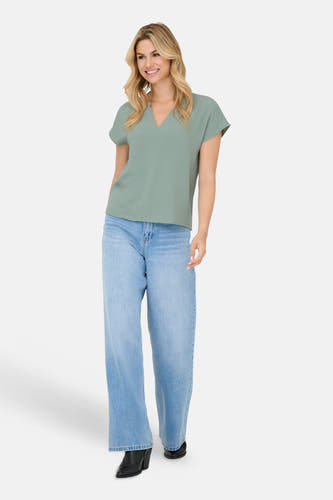 Chemisier vert à manches courtes de JDY, avec col en V et texture subtile, porté avec un jean bleu clair ample.