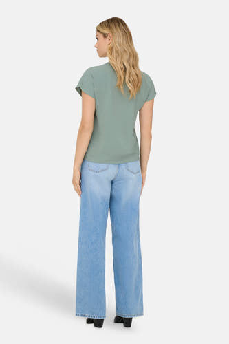 Chemisier vert à manches courtes de JDY, avec un tissu texturé, porté par un mannequin de dos avec un jean clair ample et des bottes noires.